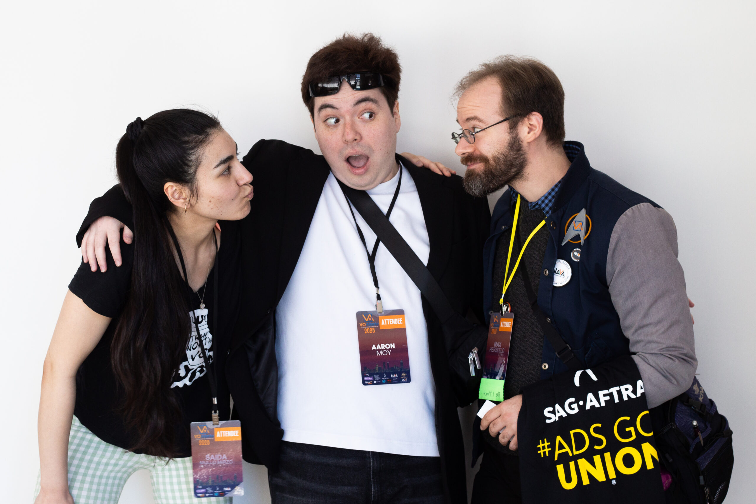 Three Attendees At Vo Atlanta 2025 Stand Closely Together Smiling And Making Playful Faces. The Person In The Middle Has A Surprised Expression, With One Arm Around Each Of The Others. All Wear Conference Badges, And The Person On The Right Carries A Sag-Aftra Tote Bag With &Quot;#Adsgounion&Quot; Written On It.