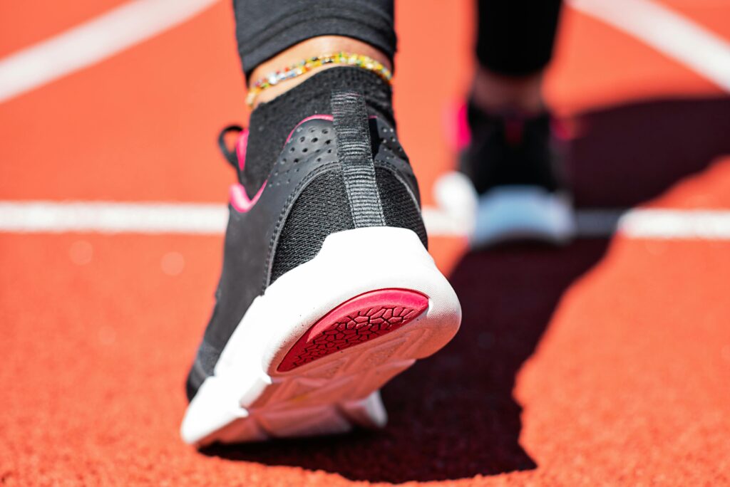 Close-Up Of A Runner’s Shoe On A Red Track, Showing The Black And Pink Sneaker With A White Sole As The Person Prepares To Step Forward.
